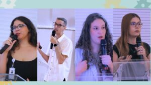 Há quatro fotos dispostas lado a lado, de pessoas falando ao microfone; a primeira foto mostra uma jovem de cabelos pretos e ondulados, usando óculos e um vestido preto. A segunda foto é de um homem de cabelos grisalhos, usando óculos e uma camisa social branca. A terceira foto é de uma mulher de cabelo loiro cacheado, usando uma blusa bege. A última foto é de uma mulher de cabelo castanho arruivado, usando óculos e uma blusa preta.