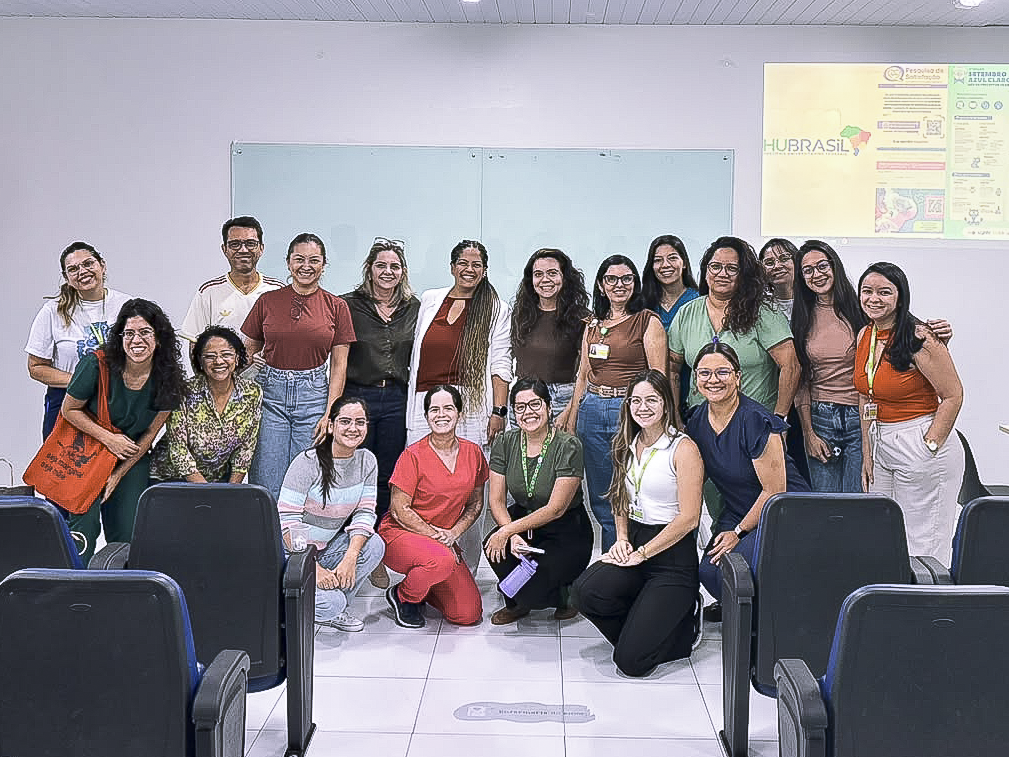 A imagem mostra um grupo de participantes, docentes e preceptores reunido na frente da sala ao final da atividade, sorrindo e posando para uma foto coletiva. Ao fundo, a tela projetada exibe conteúdos institucionais e informativos.
